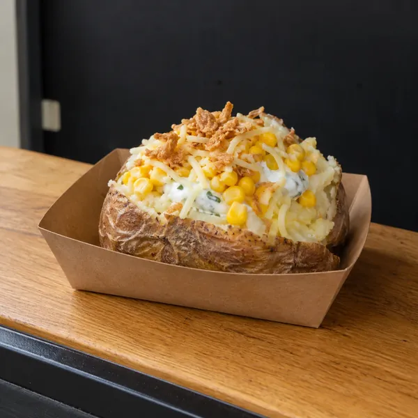 Gefüllte Ofenkartoffel mit Mais und weiteren Toppings in einer Pappschale