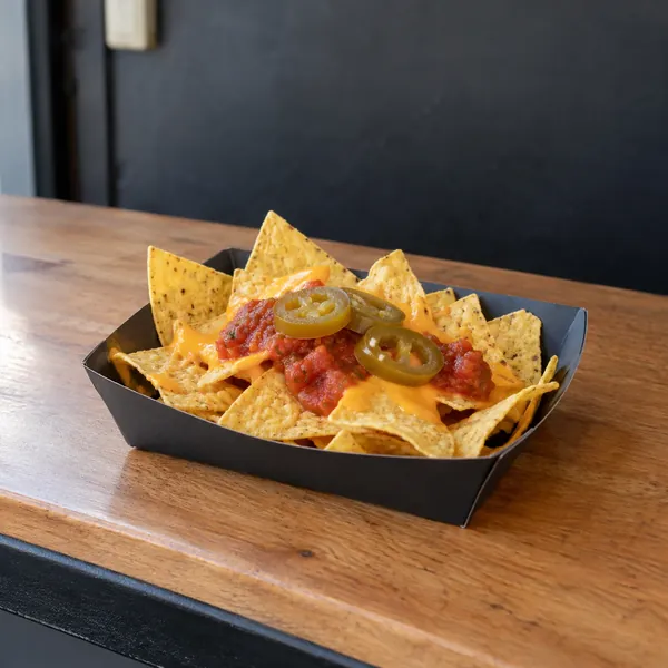 Nachos mit Käsesauce, Salsa und Jalapeños in einer dunklen Schale